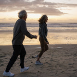 Älteres Paar beim Spaziergang am Meer bei Sonnenuntergang – Sinnbild für Langlebigkeit, Gesundheit und Lebensqualität.