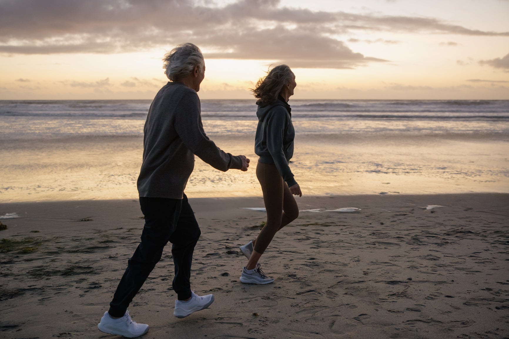 Älteres Paar beim Spaziergang am Meer bei Sonnenuntergang – Sinnbild für Langlebigkeit, Gesundheit und Lebensqualität.